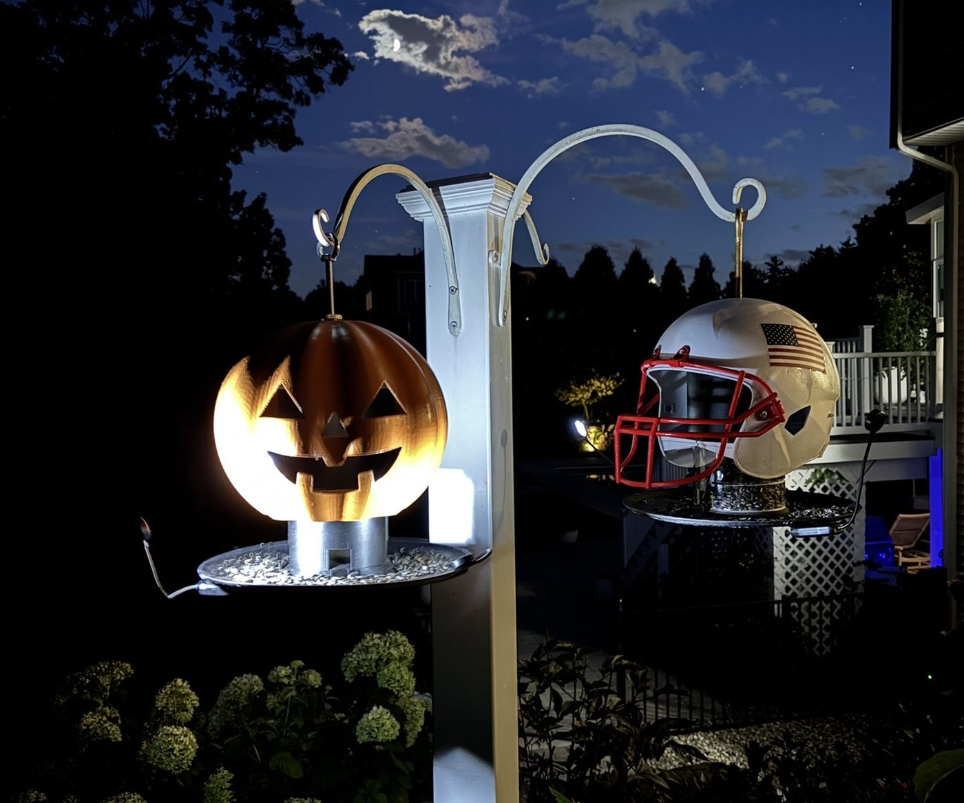 Jack the jack-o-lantern pumpkin bird feeder glowing on a pole after dark, next to the Stars and Stripes football helmet inspired bird feeder